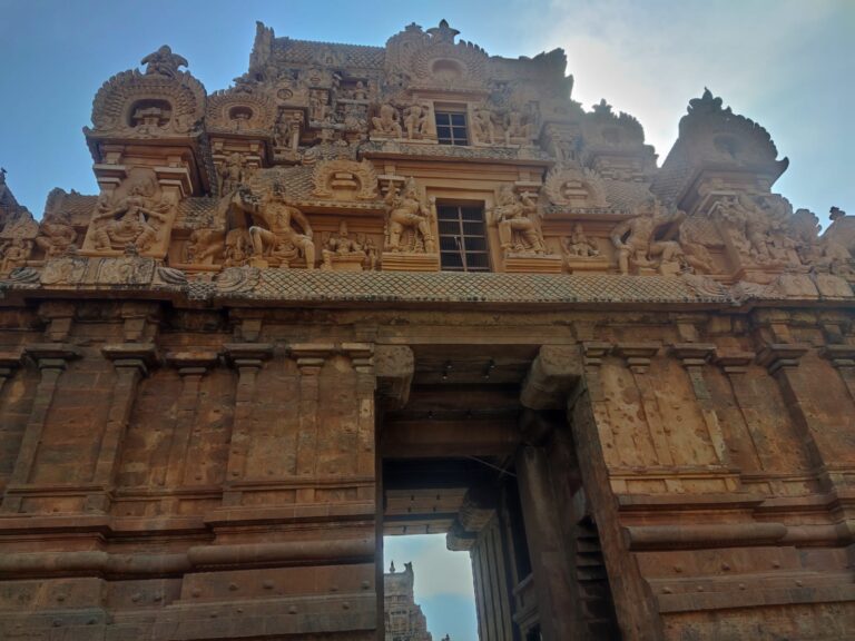 A close-up view of the stone entrance gopuram gate (Rajarajan Tiruvasal) at Brihadeeswarar Temple, highlighting detailed relief sculptures of fierce dvarapala guardians and traditional Chola architectural details above the main archway.